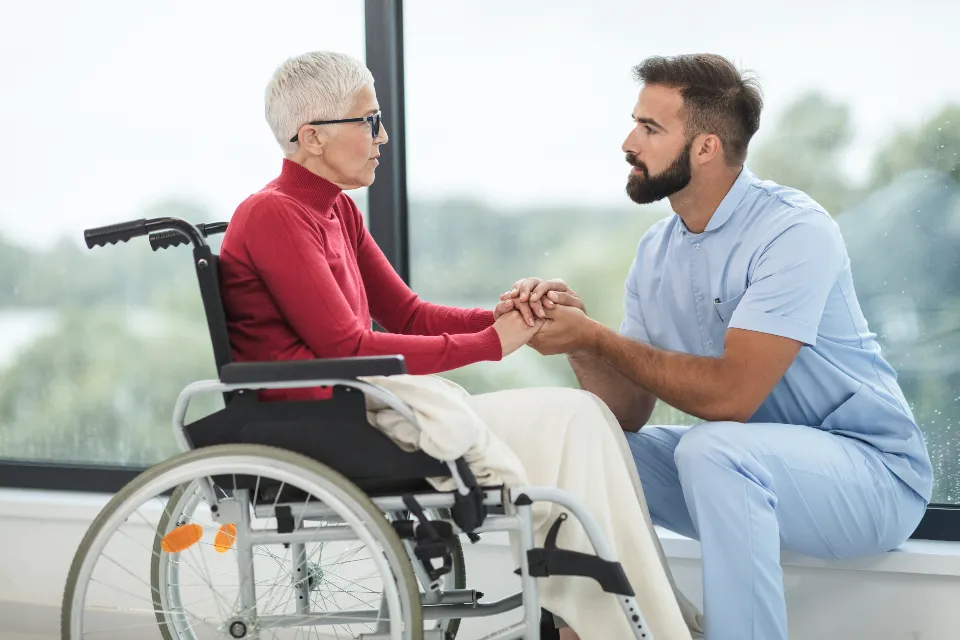 A caregiver kneeling beside a smiling woman in a wheelchair